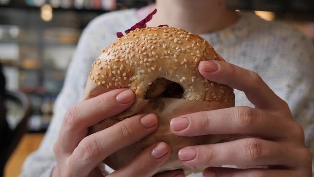 Bagel sandwich closeup woman holds and eat brunch food in the morning sitting in cafe