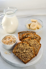 Sliced banana bread with coconut and milk on a light gray background. Homemade delicious pastries. Side view, close- up, copy space.