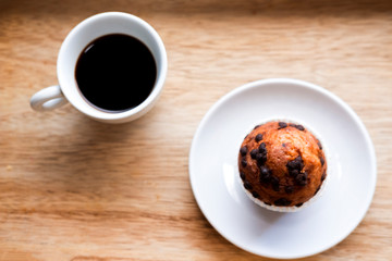 Coffee in white cup and cupcake in white plate on a wooden table for breakfast in the morning