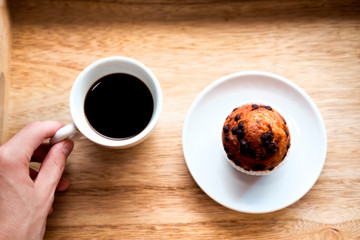 Coffee in white cup and cupcake in white plate on a wooden table for breakfast in the morning