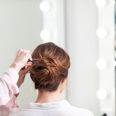 Fototapeta premium The work of the stylist on hairstyles in a bright salon, the girl makes curls and a bunch of beautiful model