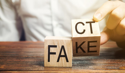 A man puts wooden blocks with the words Fact and fake. Concept of news and false information....