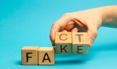 A man puts wooden blocks with the words Fact and fake. Concept of news and false information. Yellow press.