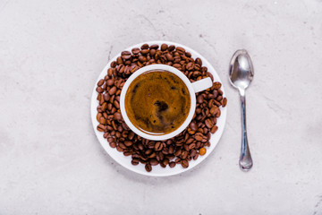 Cup of coffee, saucer with coffee beans and a spoon on a concrete surface