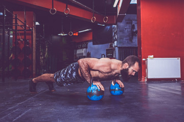Young bearded man with naked torso doing push ups with kettlebell weights