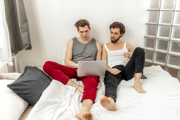 beautiful caucasian homosexual couple, gays spend time together at home, sit on bed using laptop. unusual alternative relationships, gays, homosexuality, lgbt concept