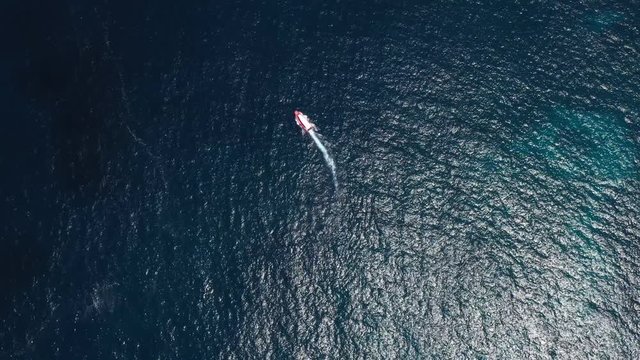 Top view from above boat anchored yacht floating in ocean runabout or cruiser stands in azure sea waters with coral reef visible. Weekender from drone beautiful weather with calm sea and sun shining