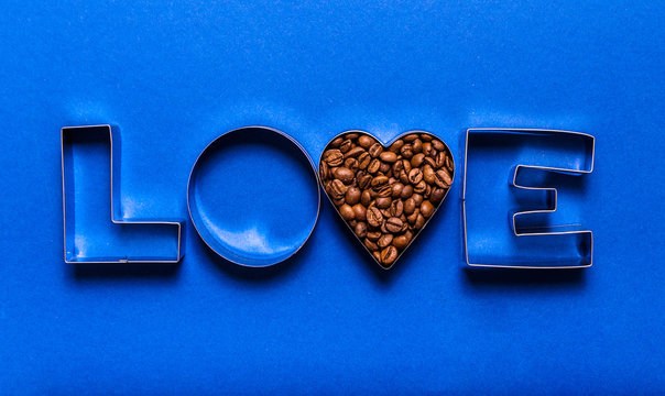 Metal letters for baking and coffee beans in the shape of a heart on a blue background. Coffee love concept
