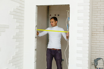 Master builder in uniform of measuring distances on a white wall with a tape measure