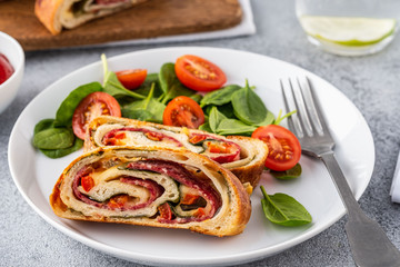 Italian food Pizza roll stromboli with cheese, salami, spinach and red pepper a light background.