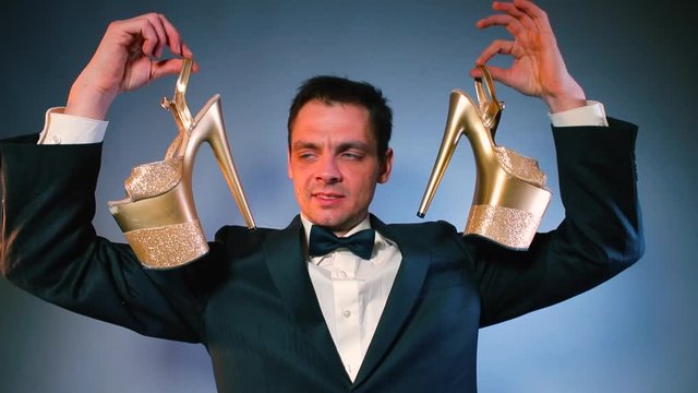 A man in a suit holds in his hands high-heeled shoes and examines them. The concept of an online store.