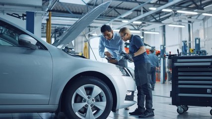Manager Checks Tasts on a Tablet Computer and Explains an Engine Breakdown to an Female Mechanic. Car Service Employees Inspect Car's Engine Bay with a LED Lamp. Modern Clean Workshop. - Powered by Adobe