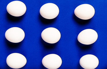 White chicken eggs are arranged in rows against a dark blue background.