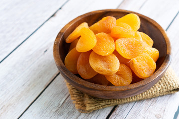 Heap of dried apricots in wooden bowl on wooden background, close up.