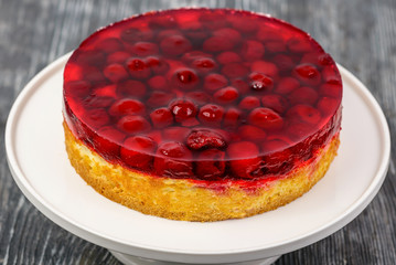 Dessert biscuit cake with cream and cherries in jelly on a white stand