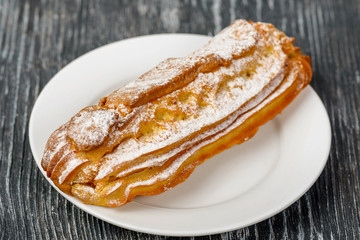 A custard eclair cake with cream filling and powdered sugar on a white plate