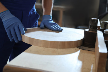 Professional carpenter grinding piece of wood in workshop, closeup