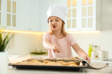 Little girl wearing chef hat baking cookies in kitchen