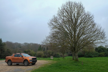 Pick up truck parked in a European natural landscape in Normandy, France under a grey sky.