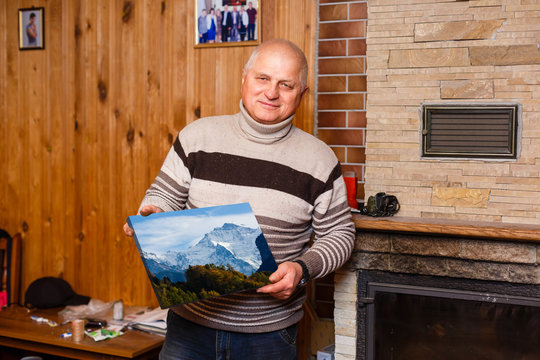 elderly man holding a photo canvas in a wooden house