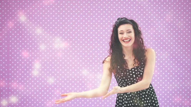 Lovely young girl with kinky hair, in black polka-dots dress dancing, waving comically her hands, pointing at copy space for text or product.