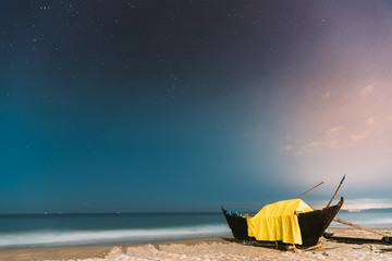 Goa, India. Real Night Sky Stars. Natural Starry Sky Blue Color Above Sea Seascape Ocean Beach. Background. Parked Old Wooden Boat At Coast
