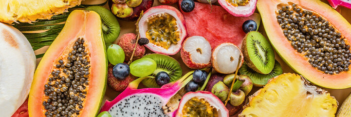 Fresh exotic fruits and tropical palm leaves on pastel orange background - papaya, mango,...
