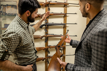 young salesman, consultant help customer to choose weapon in gun store. firearm, defense, weapons,...
