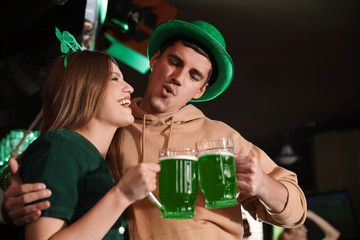 Young woman and man toasting with green beer in pub. St. Patrick's Day celebration