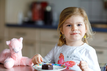 Cute funny toddler girl eating chocolate ice cream at home. Happy healthy baby child feeding plush lama toy with sweet ice-cream. Lovely kid enjoying dessert pudding. © Irina Schmidt