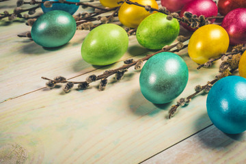 Easter festive greeting card with colored Easter eggs and willow twigs on painted wooden background close-up. Holiday background. Warm toning. Retro toned image. Selective focus, copy space.
