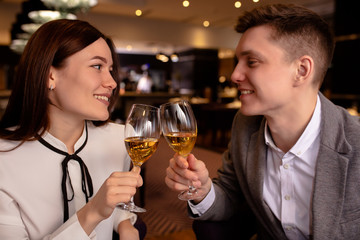 young beautiful caucasian couple celebrate anniversary in luxury rich restaurant, they sit and look at each other with love, clink glasses with champagne