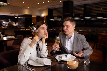 bored caucasian lady with champagne and handsome male entertaining her. gentleman in love with her, while female is not interested in rendezvous with him. they sit in luxury restaurant