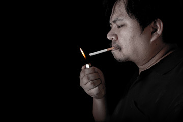 Fototapeta premium The fat man lighting up a joint with lighter smoking at the black background, close up image of cigarette smoke spread in hand