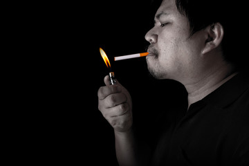 Fototapeta premium The fat man lighting up a joint with lighter smoking at the black background, close up image of cigarette smoke spread in hand