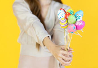 A beautiful young asian woman with smiling face wearing bunny ear, holding multicolored set of easter eggs on the yellow baclground