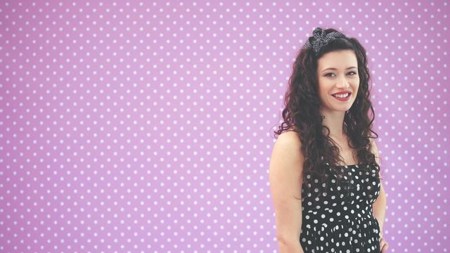 Beautiful young girl with kinky hair wearing nice black polka-dots dress is standing in profile, then turning, looking at the camera, smiling.