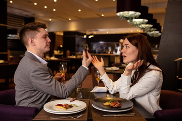 dissatisfied caucasian woman and handsome guy in restaurant. couple have quarrel, offended man and woman sit together, discuss relationships problems. man hold smartphone