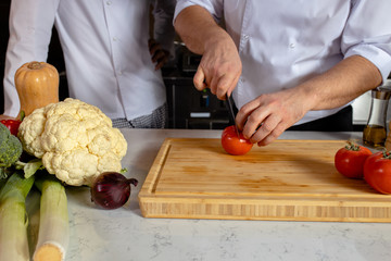 chef-cooker cut fresh vegetables on wooden board in kitchen, professional cook work in restaurant. man in apron