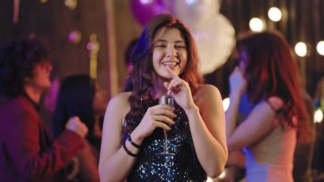Smiling attractive young woman ina glamorous dress at big party in front of the camera enjoying the time at party drinking champagne and feeling relaxed. Shot on ARRI Cinema Camera
