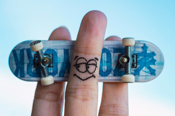 Fingers with a painted face playing with a small skateboard   © Laura