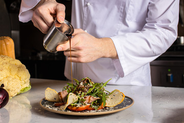 professional chef-cook gently pour the sauce on the salad in the kitchen. cropped man in apron make vegetarian salad dish for restaurant visitors