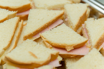 Many sandwiches on a steel tray. Many Panini stacked with ham and cheese