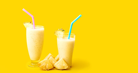 Fresh pineapple smoothie in two glasses and pineapple slices on a yellow background. Space for text