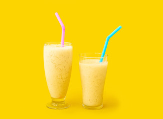 Fresh pineapple smoothie in two glasses on a yellow background