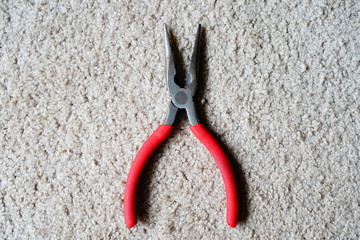 Red handle needle nose pliers laying on a carpeted floor