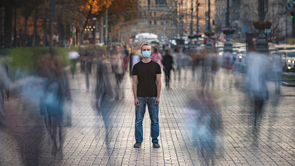 The young man with medical face mask stands on the crowded street