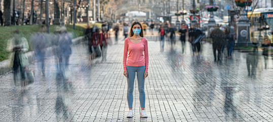 The young woman with medical mask on her face stands on the crowded street