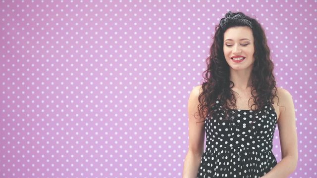 Beautiful young girl with kinky hair and black headband, wearing nice black polka-dots dress is pointing at copyspace for text or product.