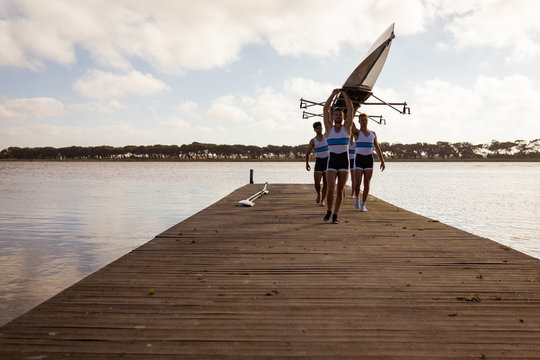 Teammates carrying rowing boat together while walking on pier